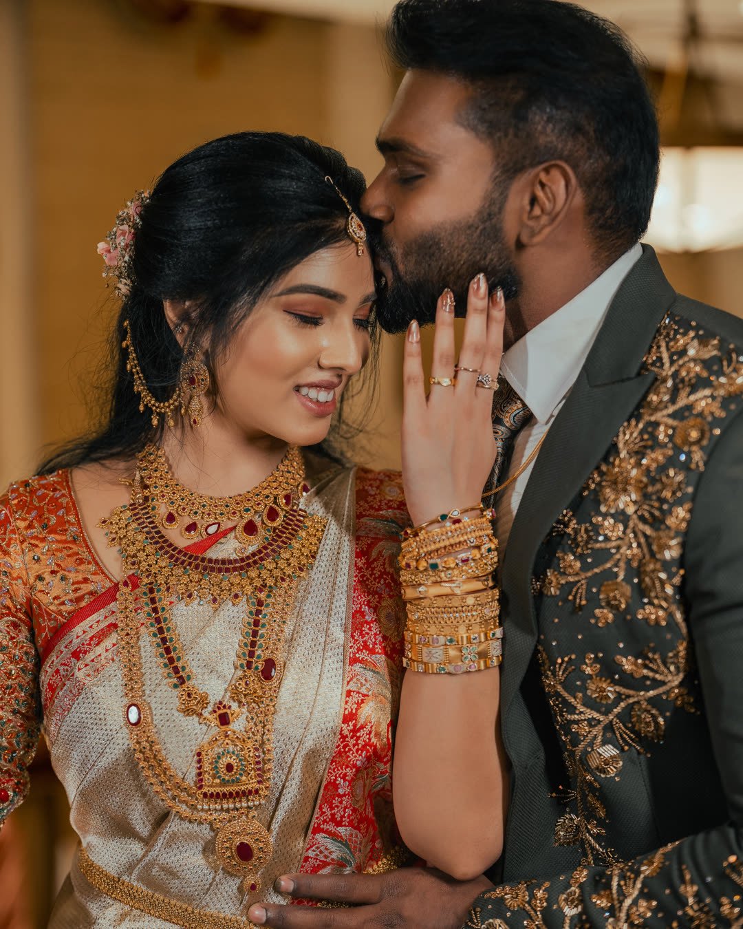 Bride in a red and gold sari smiling as her groom holds her hand